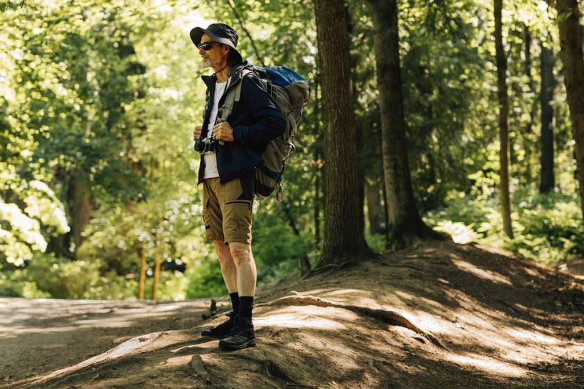 man standing in woods dressed for a hike on sunny day